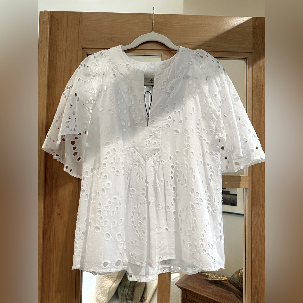 White eyelet blouse with oversized flutter sleeves and a v-neckline.